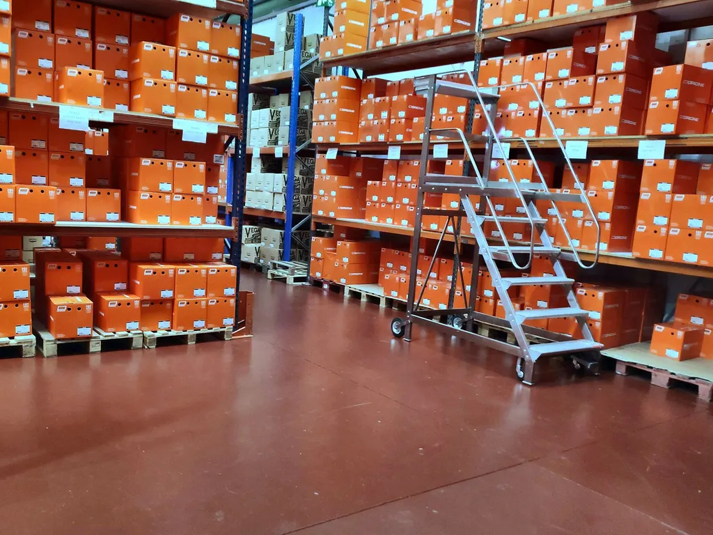 Cajas de producto sobre palés y estanterías, con una escalera móvil para acceder a los niveles altos