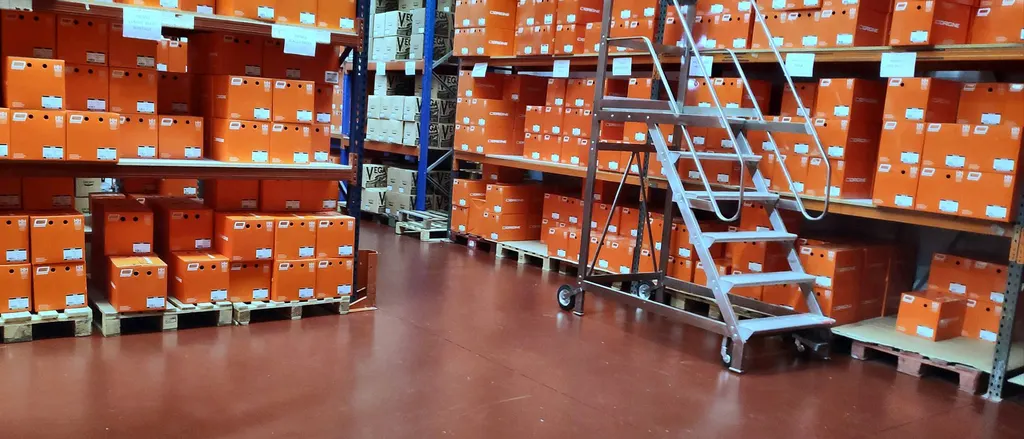 Product boxes on pallets and shelving, with a mobile ladder to reach the upper levels