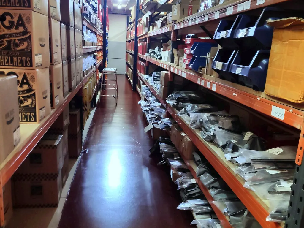 Pasillo de preparación con ubicaciones etiquetadas, cajas de cascos y recambios embolsados por referencia